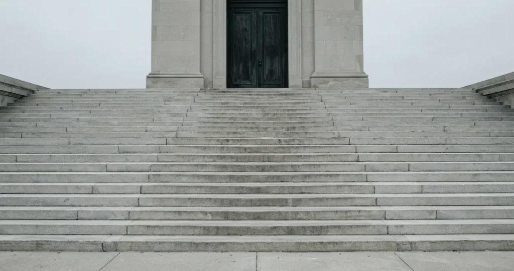 Empty stone courthouse steps leading to closed dark doors under a grey sky — visualising the gap between the promise of justice and its delivery in To Kill a Mockingbird